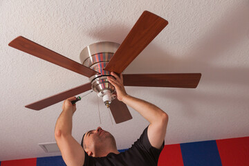 Man installing a ceiling fan in a bedroom