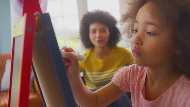 Mother in wheelchair watching daughter having fun drawing picture on whiteboard at home- shot in slow motion