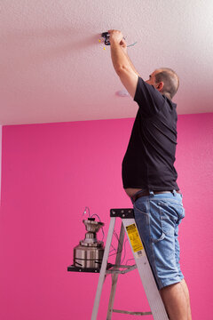 Man Installing A Ceiling Fan In A Bedroom