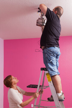 Man Installing A Ceiling Fan In A Bedroom