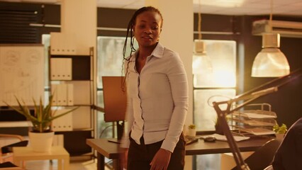 Company worker waving goodbye at coworker leaving office, finishing charts presentation on computer. Working on business project with research to create online data report during sunset.