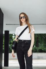 Cheerful hipster girl with sunglasses walking in the urban city street. White t-shirt and black trousers