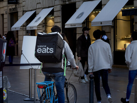 BORDEAUX, FRANCE - FEBRUARY 25, 2022: Uber Eats logo on the bag of a delivery man on his bicycle, riding in a crowd of people in bordeaux to deliver a food order from a restaurant.....