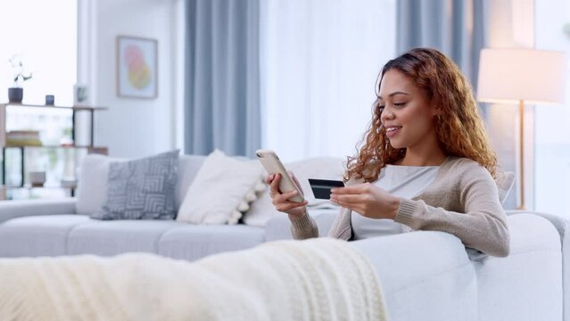 Credit card holder making online purchase on her phone on a sofa. Happy woman applying for a loan via a digital banking app. Female paying off insurance debt with modern tech and feeling satisfied