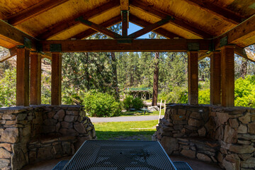 View of the small pond area and waterfall from a covered wooden log picnic and BBQ gazebo clubhouse at Mirabeau Park in Spokane Valley, Washington.