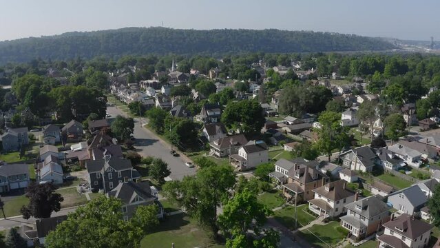 A slow orbiting summer aerial establishing shot of a small Pennsylvanian town. The Beaver County Shell cracker factory on the Ohio River in the distance.  	