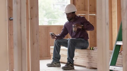 Break time! Contractor takes a break while he sips on his coffee and scrolls through his social media. - Powered by Adobe