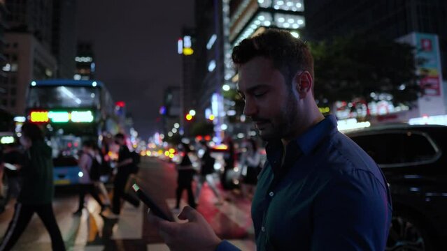 Man gets a worried upset face using his phone on a crowded crosswalk at night in Gangnam Station district, Seoul South Korea