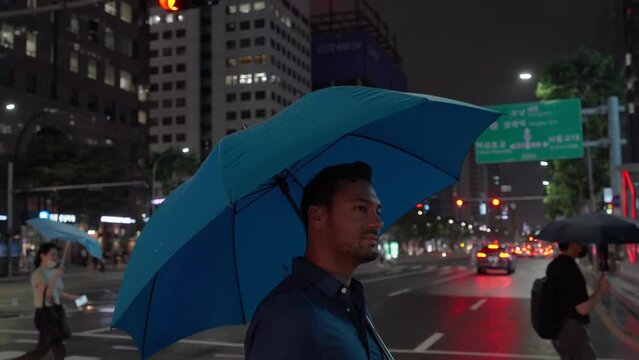 Tracking shot of a bearded young man with Umbrella walking on zebra in Downtown Seoul at night - slow motion