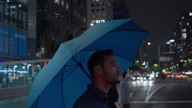 Man with umbrella crossing Gangnam street road at night, Seoul South Korea