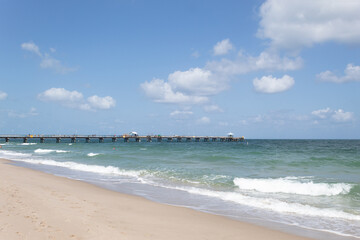 Fototapeta na wymiar Beach on a sunny day with a calm sea, a sky with few clouds and a pier on the horizon line