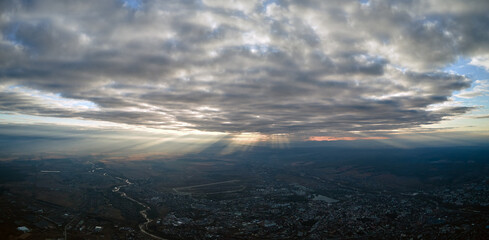 Aerial view from airplane window at high altitude of distant city covered with puffy cumulus clouds forming before rainstorm