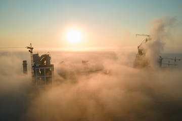 Fototapeta premium Aerial view of cement factory with high concrete plant structure and tower crane at industrial production site on foggy morning. Manufacture and global industry concept