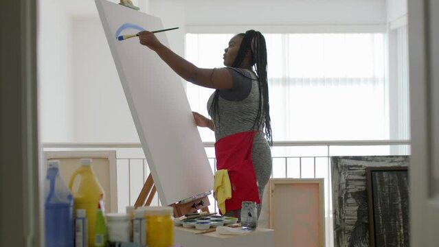 A young black female artist paints a beautiful canvas in her studio. 