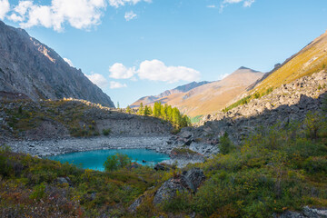 Fototapeta na wymiar Pure turquoise alpine lake among lush autumn vegetation with view to large mountains in sunlight. Beautiful glacial lake against sunlit pyramid shaped mountain. Vivid autumn colors in high mountains.