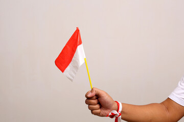 Hand's man holding indonesian flag with red whit ribbon on the wrist. Isolated on gray background