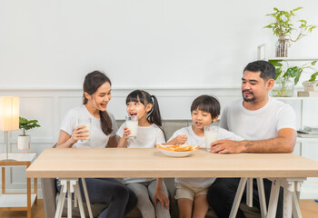 Asian  family enjoying breakfast at living room. little girl daughter sitting on table, drinking milk with smiling father and mother in morning. Happy family at home.