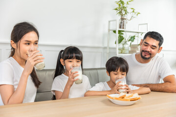 Asian  family enjoying breakfast at living room. little girl daughter sitting on table, drinking milk with smiling father and mother in morning. Happy family at home.