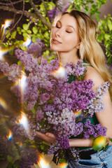 Fototapeta premium a beautiful woman in a green top and jeans with lilac flowers. solar flare.