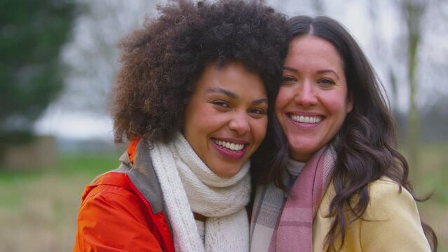 Head and shoulders portrait shot of loving same sex female couple hugging on outdoor walk in autumn countryside together