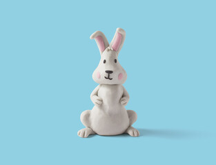 Cute sitting rabbit made of white plasticine on a blue background. Handmade easter rabbit in clay. 3d artwork
