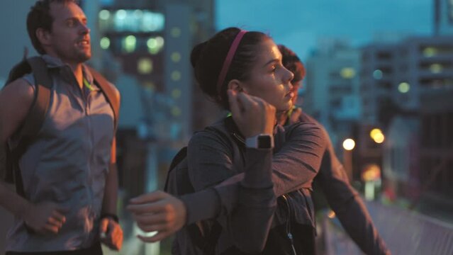 Fitness group stretching for a city night jogging session together. Fit running team training for a serious sport workout. Closeup view of a healthy woman runner ready to exercise in the dark.