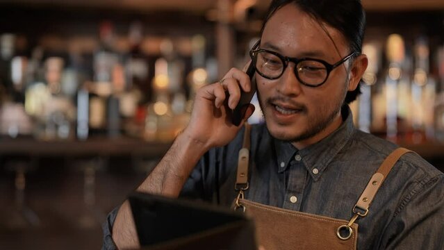 Night club concept of 4k Resolution. The bartender is taking orders from customers with the phone in the restaurant. A group of specialized clubs that sell alcoholic beverages.