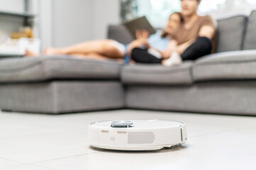 Fototapeta premium Young couple resting on the couch while robotic vacuum cleaner doing its work at home. Household robots, Smart home concept