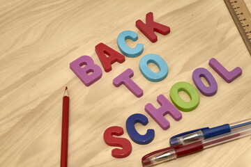 the phrase back to school is laid out in multicolored letters on the table next to colored pencils fountain pens and a ruler the concept of education school