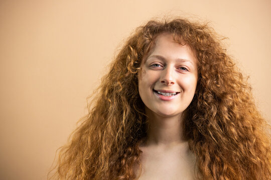 Close up pfoto of a beauty smiling widely redhead young woman with naked breast posing at the camera over golden background.
