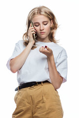 Sad girl speaks on the phone. A teenager in beige trousers and a white T-shirt. Frustration and bad news. White background. Vertical.