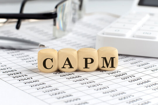 wooden cubes with the word CAPM on a financial background with chart, calculator, pen and glasses, business concept.