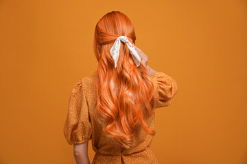 Beautiful woman with long orange hair on color background, back view