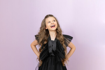 A happy little girl with wavy hair in a black dress on a pink isolated background. A beautiful...