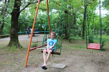 a boy walks in the woods in the summer and rides on a swing