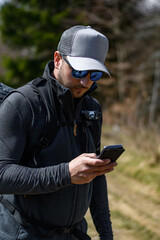 junger Mann mit Basecap schaut in der Natur auf sein Smartphone