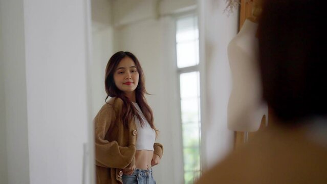 Young beautiful asian woman happily dressed in front of the mirror. She looks good and has confidence in herself
