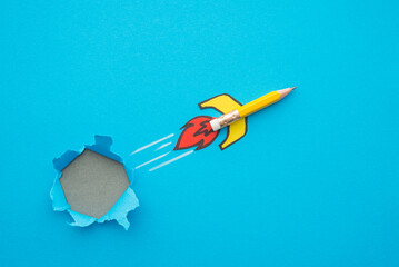 Yellow pencil rocket breaking through hole from obstacle wall to blue zone background minimal style. Concept of breakthrough for new idea, innovative, successful goal in business financial education.