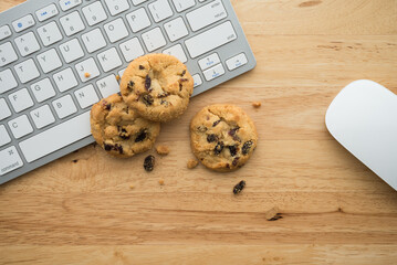Flat lay of white chocolate chip cookies on keyboard computer and mouse on wooden table background...