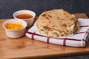 Pupusas on a wooden board with curtido and sauce over a black marble background