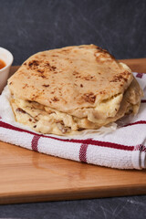 Pupusas on a wooden board with curtido and sauce over a black marble background