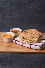 Pupusas on a wooden board with curtido and sauce over a black marble background
