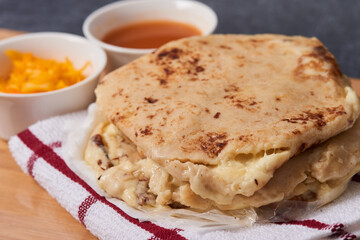 Pupusas on a wooden board with curtido and sauce over a black marble background