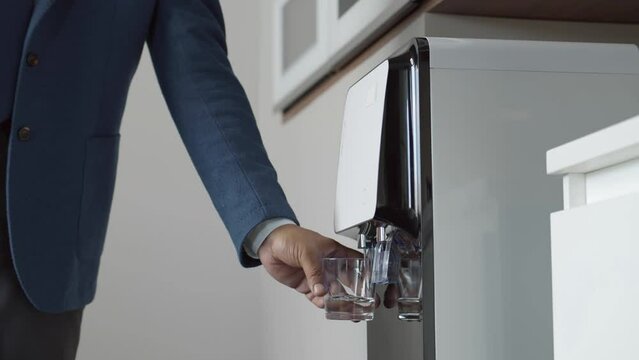 Cropped shot of businessman pouring water from cooler in office. Realtime