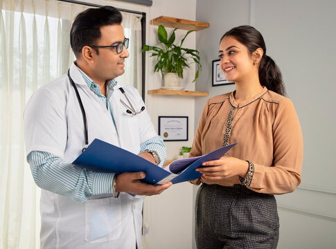 Asian Indian man or male physician or doctor wearing stethoscope and apron holding report file in hand and giving consultation to a smiling female or happy Woman patient. Medical, medicine, healthcare - Powered by Adobe