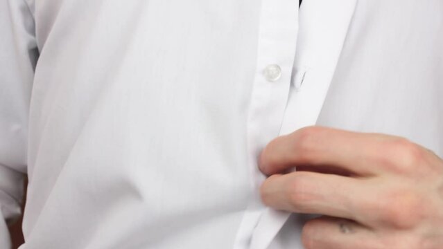 A man undoes the buttons on a white shirt.Take off the shirt.Men's button down shirt.Classic office shirt.