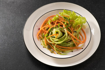 fresh vegetable salad of carrots with cucumber on a white dish and a gray background, serving, close-up