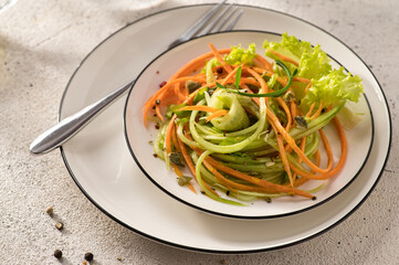fresh vegetable salad of carrots with cucumber on a white dish, with a fork, light background, close-up, top view