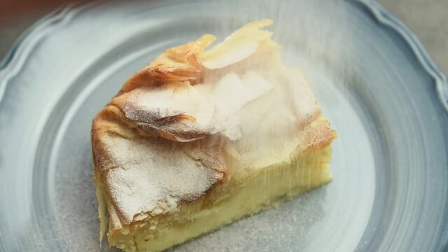 The confectioner sprinkles powdered sugar on a piece of Greek custard pie.
