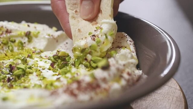Dipping a piece of bread in homemade labneh with pistachios.
